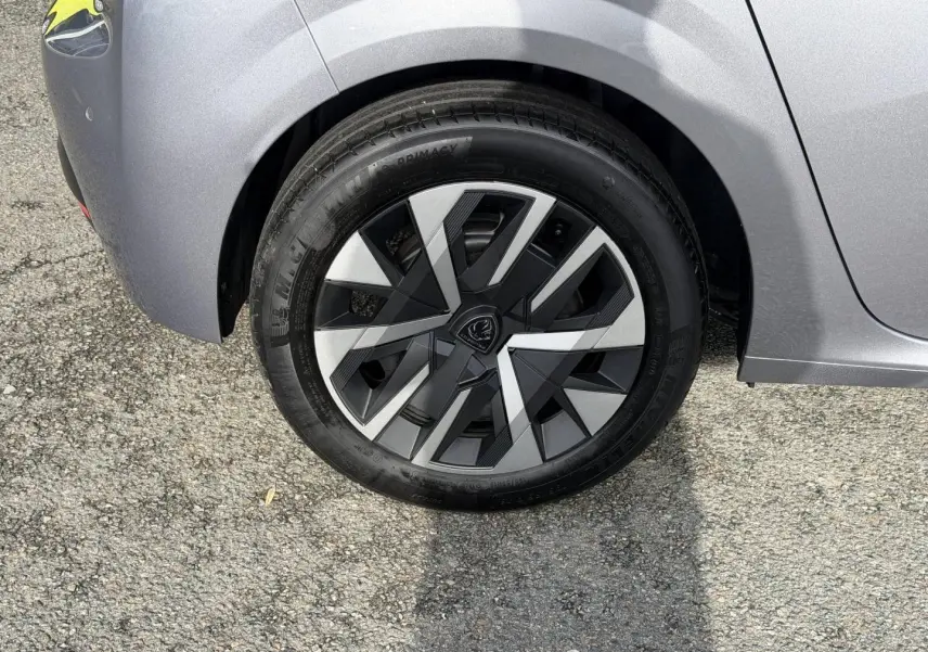 Gros plan sur la roue arrière droite d'une Peugeot 208 1.2 Hybrid gris Artense avec jante au design géométrique noir et argent.