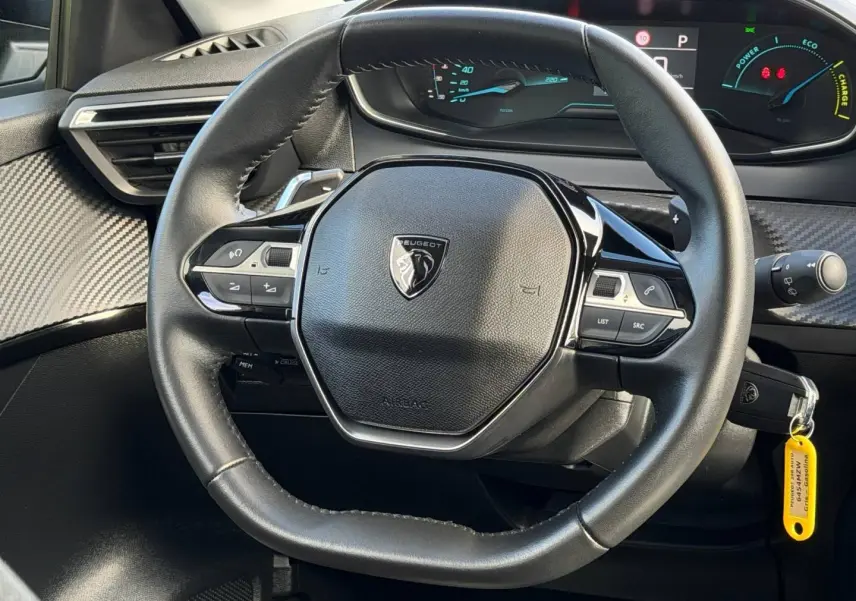 Vue rapprochée du volant noir de la Peugeot 208 1.2 Hybrid 110ch avec tableau de bord numérique en arrière-plan.