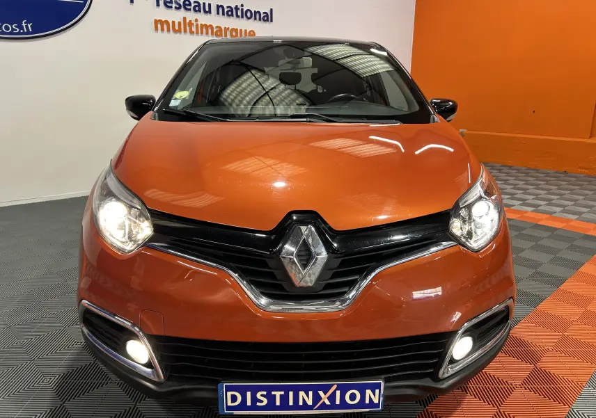 Vue frontale d'un Renault Captur orange 2014 avec phares et feux antibrouillard allumés en intérieur showroom