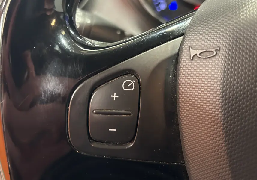 Gros plan sur les commandes de régulateur de vitesse au volant d'une Renault Captur orange de 2014.