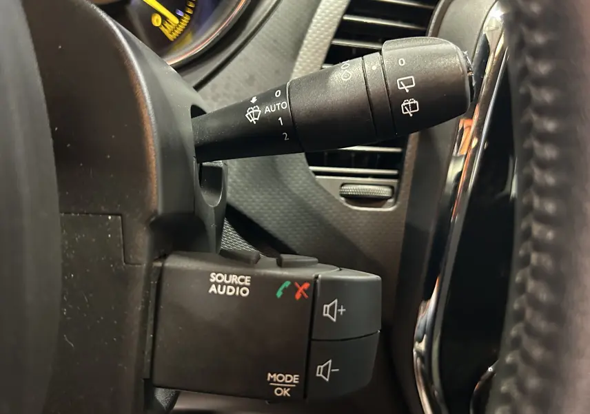 Gros plan sur les commandes au volant côté gauche du Renault Captur orange 2014, avec commandes audio et essuie-glace.