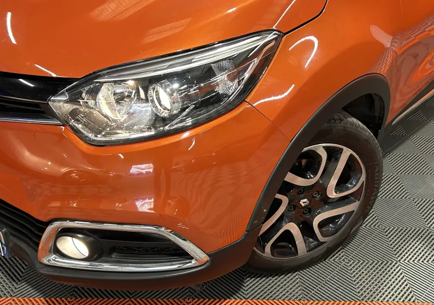 Gros plan sur l'avant droit orange du Renault Captur 2014, mettant en valeur le phare et la roue alliage noire et argent.