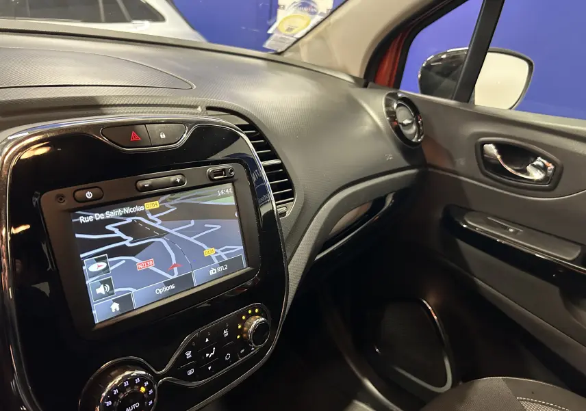 Vue intérieure côté passager du tableau de bord du Renault Captur orange de 2014 avec écran GPS allumé et commandes de climatisation.