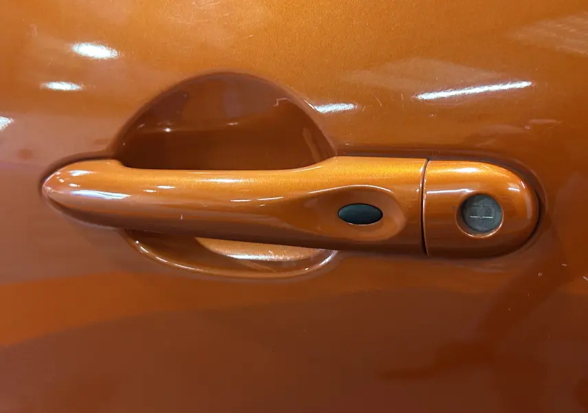 Poignée de porte orange métallisé du côté gauche d'un Renault Captur dCi 90ch energy Intens 2014 avec bouton noir et serrure visible.