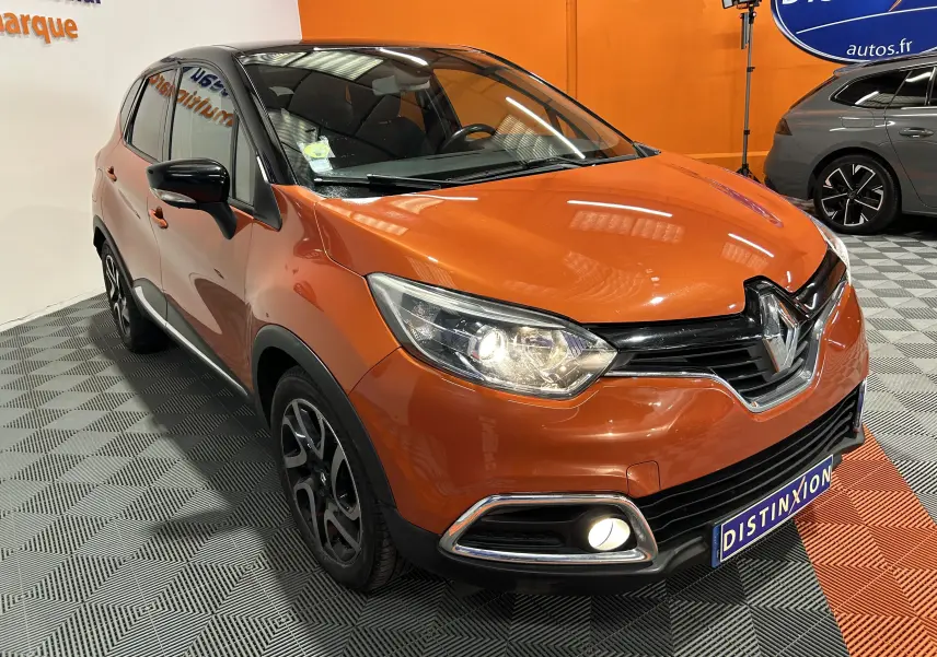Renault Captur orange vue 3/4 avant droit avec phares allumés et jantes alliage noires en showroom.