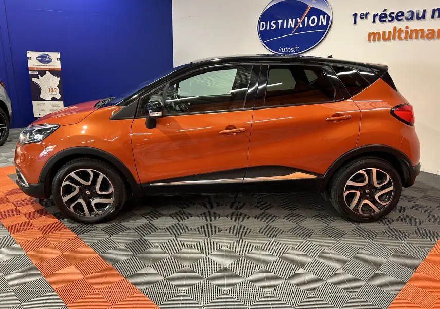 Profil latéral gauche d'un Renault Captur orange 2014 avec jantes alliage et toit noir en intérieur showroom.