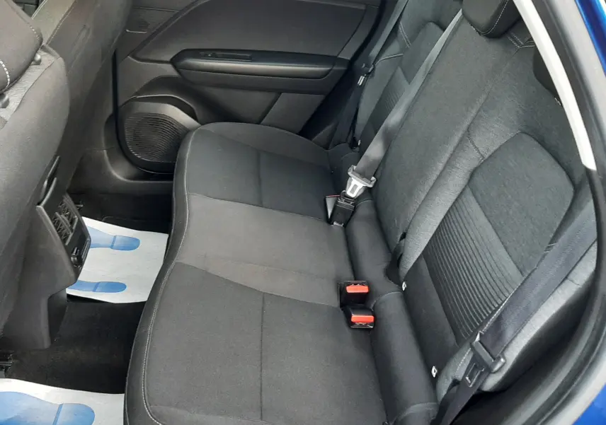 Vue intérieure arrière droite du Renault Captur bleu iron, sièges tissu noir avec ceintures de sécurité visibles.