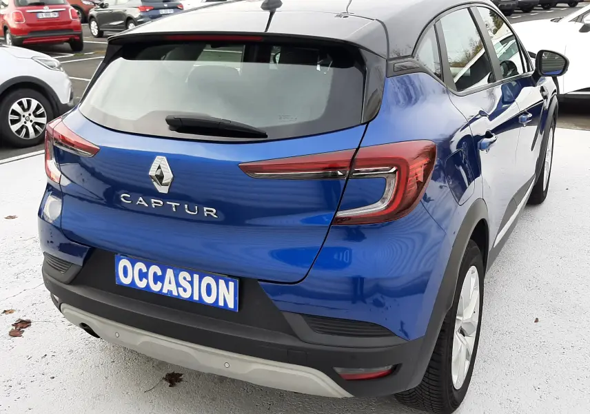 Vue 3/4 arrière droite d'un Renault Captur bleu Iron avec toit noir, sur un parking en extérieur.