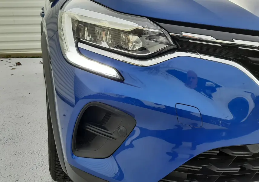 Gros plan sur l'avant gauche du Renault Captur bleu iron avec toit noir, mettant en valeur le phare LED et la calandre.