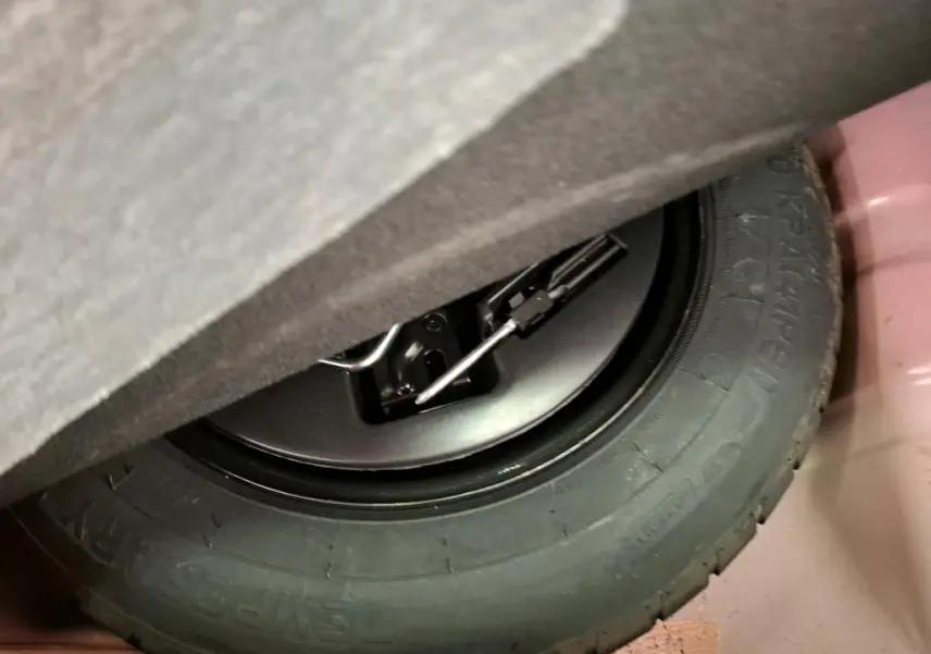 Gros plan sur la roue de secours noire et son outil de levage dans le coffre d'une FIAT 500 rouge Dolcevita 2021.