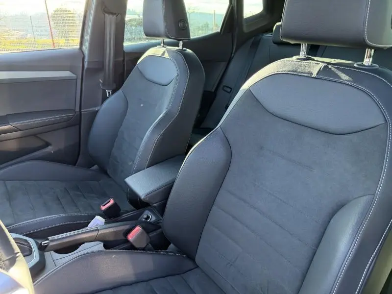 Vue intérieure rapprochée des sièges avant noirs du SEAT Arona 2025, mettant en valeur les surpiqûres blanches et l'accoudoir central.