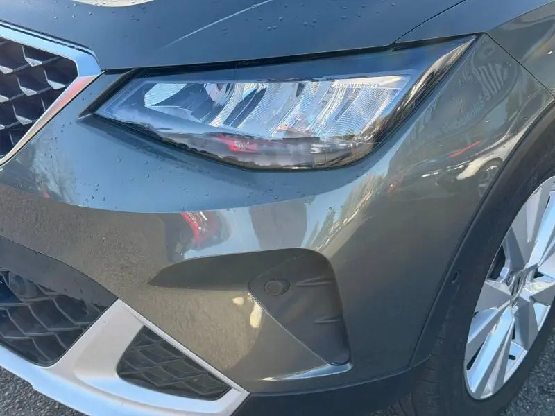 Gros plan sur l'avant droit gris métallisé du SEAT Arona 2025, mettant en valeur le phare et la calandre distinctive.