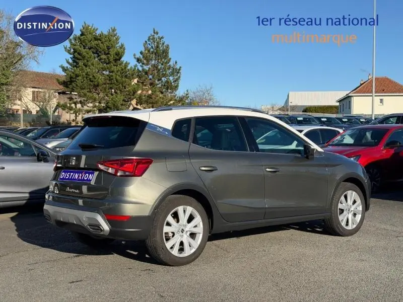 Vue 3/4 arrière droite d'un SEAT Arona gris métallisé 2025 avec toit blanc et jantes argentées sur parking extérieur.