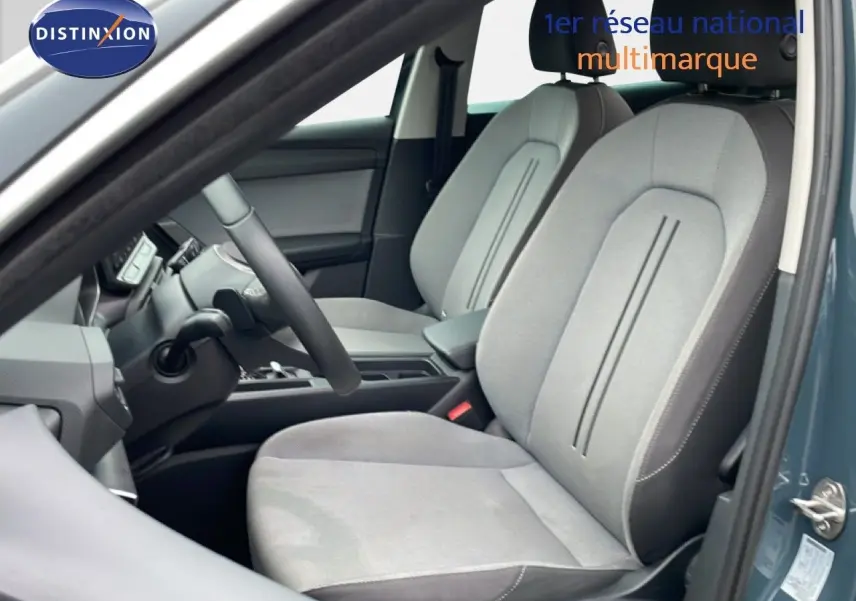 Vue intérieure côté conducteur du SEAT LEON IV 1.5TSI gris Fiord, mettant en valeur les sièges tissu gris clair et la console centrale.