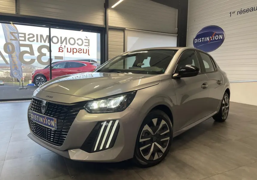 Peugeot 208 gris clair en 3/4 avant droit avec feux LED et jantes tôle 16 pouces en showroom.