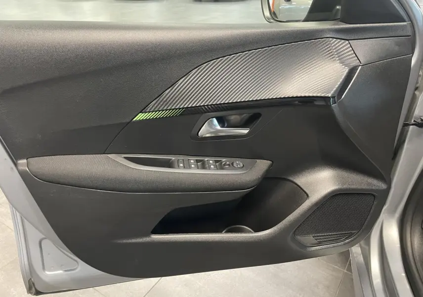 Vue intérieure de la porte avant gauche gris clair de la Peugeot 208 2024 avec insert carbone et commandes électriques.