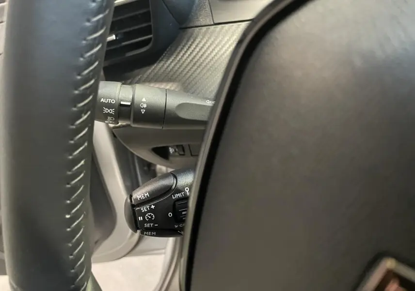 Gros plan sur la commande de régulateur de vitesse à gauche du volant cuir noir du Peugeot 208 gris clair 2024.