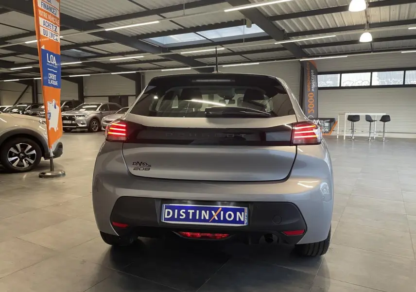 Vue arrière d'une Peugeot 208 gris clair 2024 avec feux arrière à LED et bandeau noir brillant en concession.