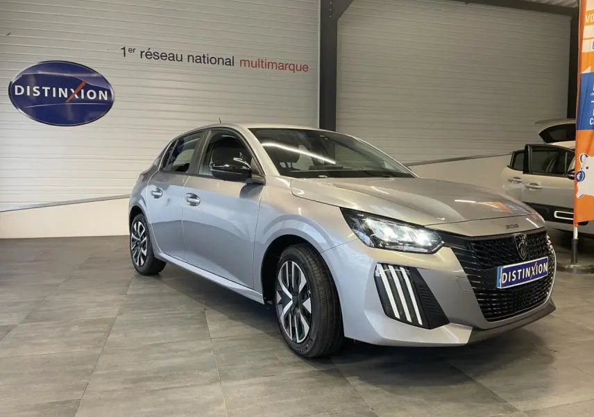 Peugeot 208 gris clair vue 3/4 avant droit en intérieur avec calandre noire et feux LED griffés.