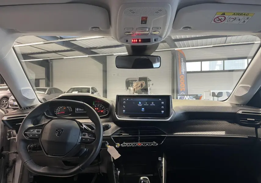 Vue intérieure frontale du tableau de bord noir et volant cuir de la Peugeot 208 1.2i PureTech 2024 avec écran tactile central.