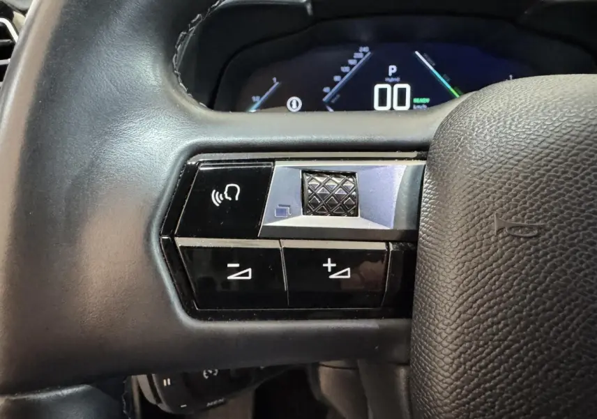 Gros plan sur les commandes gauche du volant cuir noir du DS7 Crossback E-TENSE 225 Bastille+ avec affichage digital en arrière-plan.