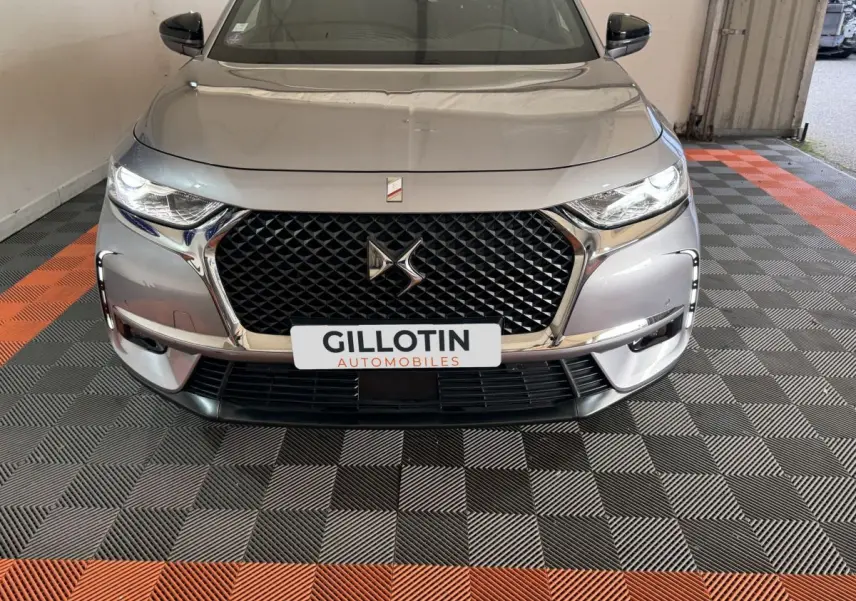 Vue avant d'une DS7 Crossback E-TENSE gris foncé avec calandre noire et phares LED allumés dans un garage.