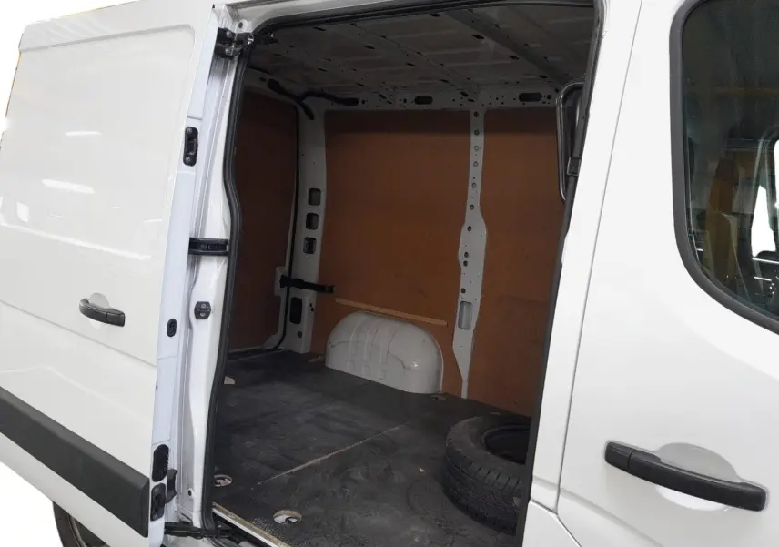 Vue latérale droite du Renault Master blanc 2023 avec porte coulissante ouverte montrant l'espace de chargement vide et une roue de secours.