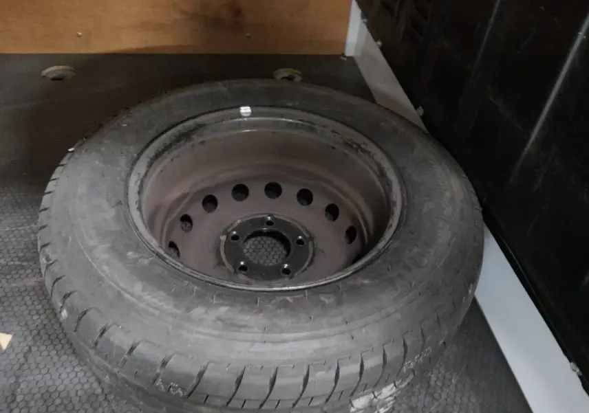 Pneu de secours noir posé dans l’espace de chargement du Renault Master blanc, vue en plongée rapprochée.