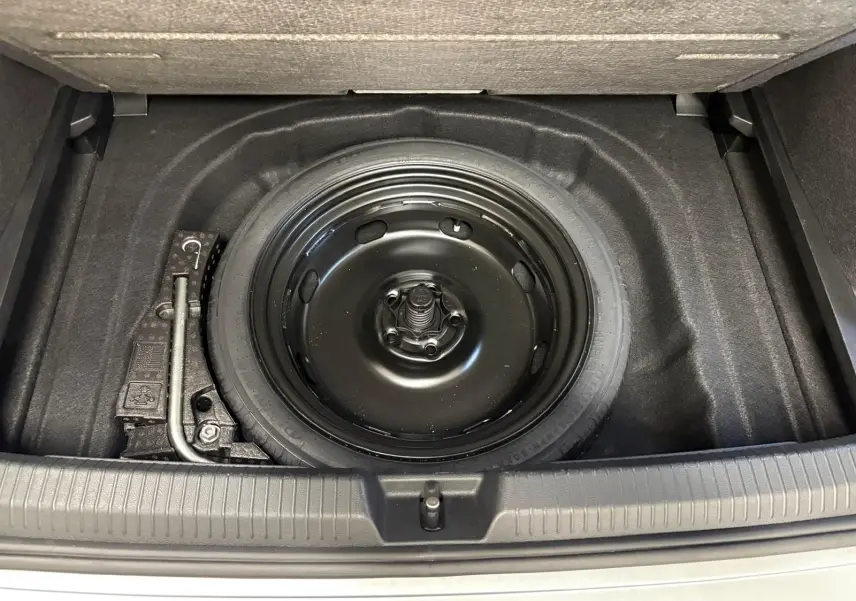 Vue plongeante sur la roue de secours noire dans le coffre d'une Volkswagen Golf 2.0 TDI 2025 couleur reflet d'argent.