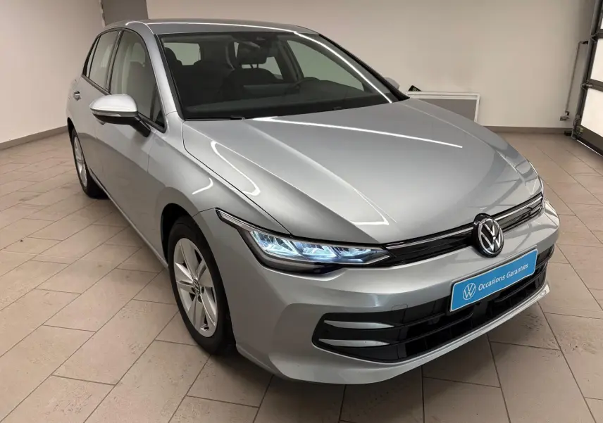 Volkswagen Golf 2.0 TDI 2025 en reflet d'argent, vue 3/4 avant droit avec phares LED allumés en intérieur.