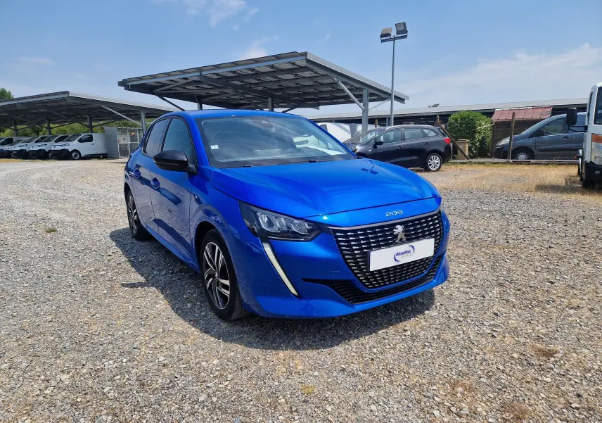 Peugeot 208 bleu Vertigo vue 3/4 avant droit sur parking, calandre noire avec logo lion et phares LED distinctifs.