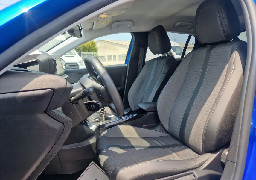 Vue intérieure côté conducteur de la Peugeot 208 bleu Vertigo 2022, montrant les sièges tissu et cuir et le volant.