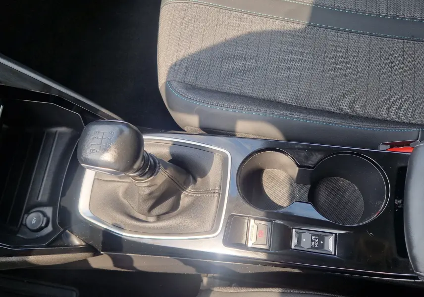 Vue rapprochée de la console centrale d'une Peugeot 208 bleu Vertigo 2022 avec levier de vitesse manuel et porte-gobelets.