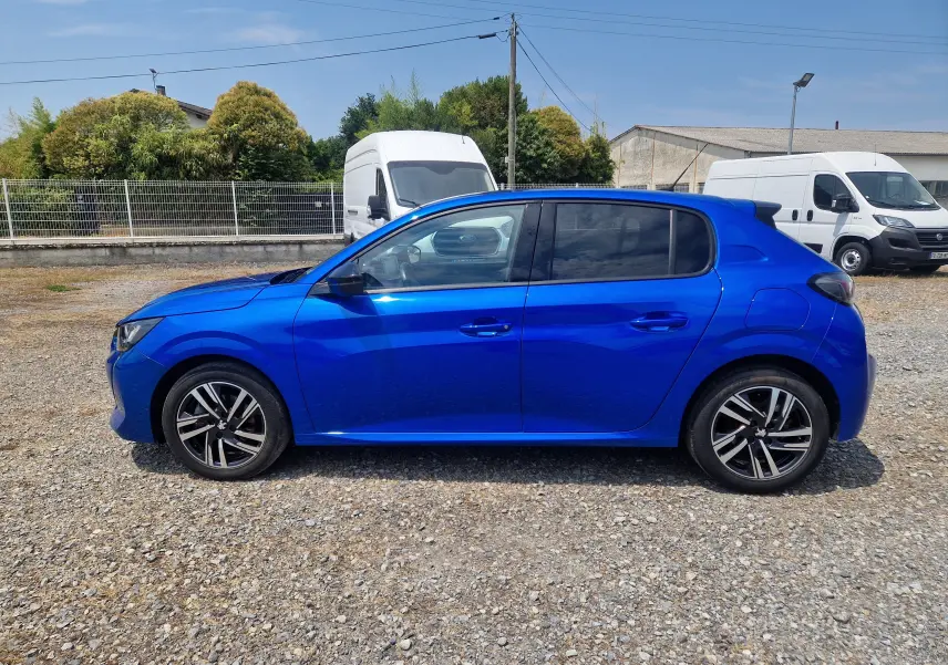 Peugeot 208 bleu Vertigo vue de profil côté gauche, avec jantes alliage et vitres teintées, sur sol gravillonné.