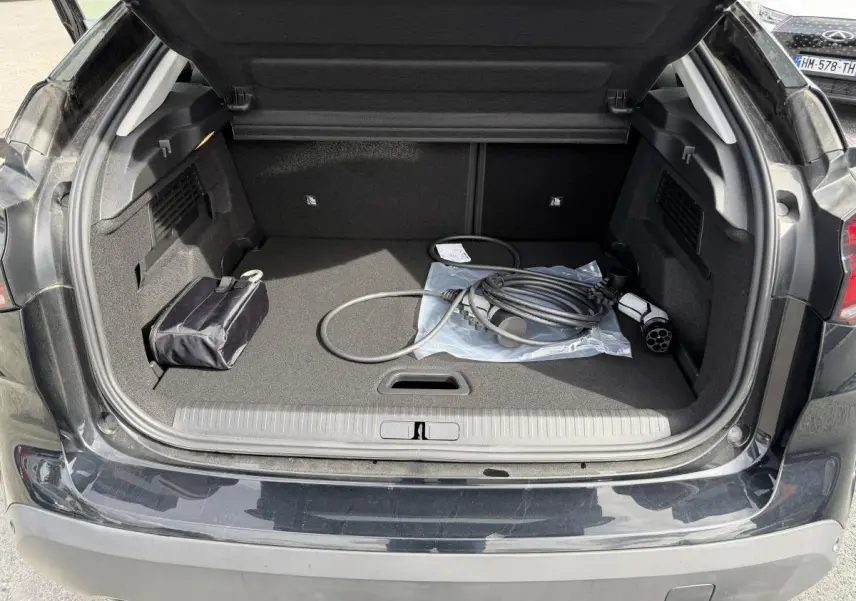 Coffre ouvert de la Citroën C4 ë-136 noir brillant, avec câble de recharge électrique visible à l'intérieur.