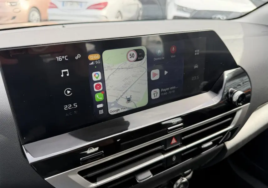 Vue rapprochée de l’écran tactile central du tableau de bord de la Citroën C4 ë-136 noir, affichant la navigation et la climatisation.