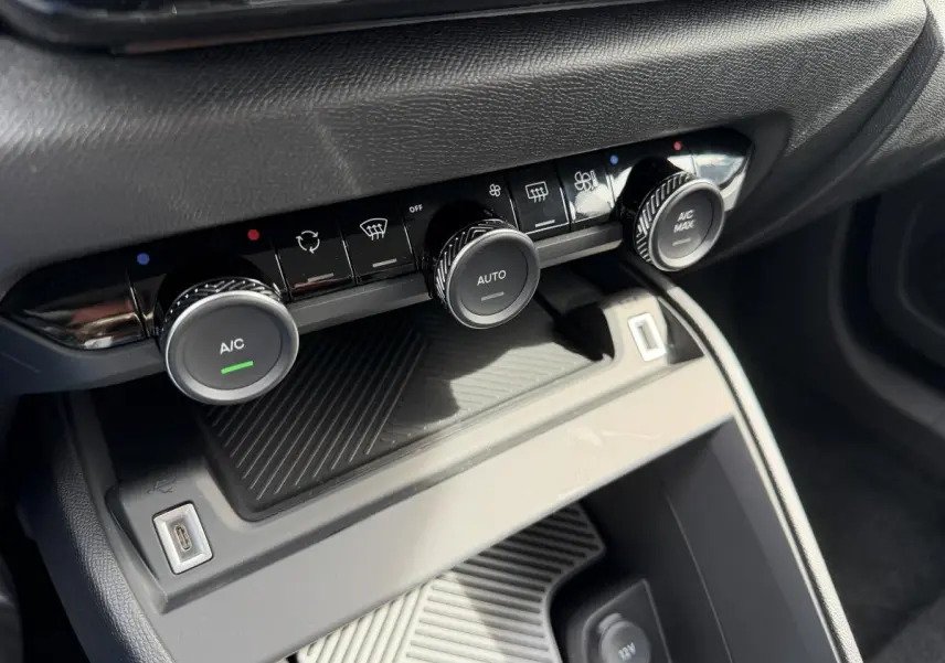 Gros plan sur la console centrale de la Citroën C4 ë-136 2025, montrant les commandes de climatisation et une prise USB.