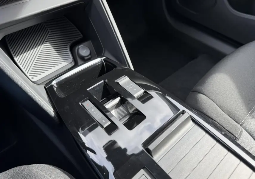 Gros plan sur la console centrale noire brillante de la Citroën ë-C4 2025 avec levier de vitesses automatique et bouton Drive Mode.