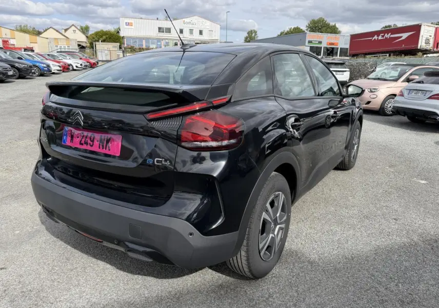 Vue 3/4 arrière droite d'une Citroën C4 ë-136 noire avec inserts noir brillant, stationnée en extérieur.