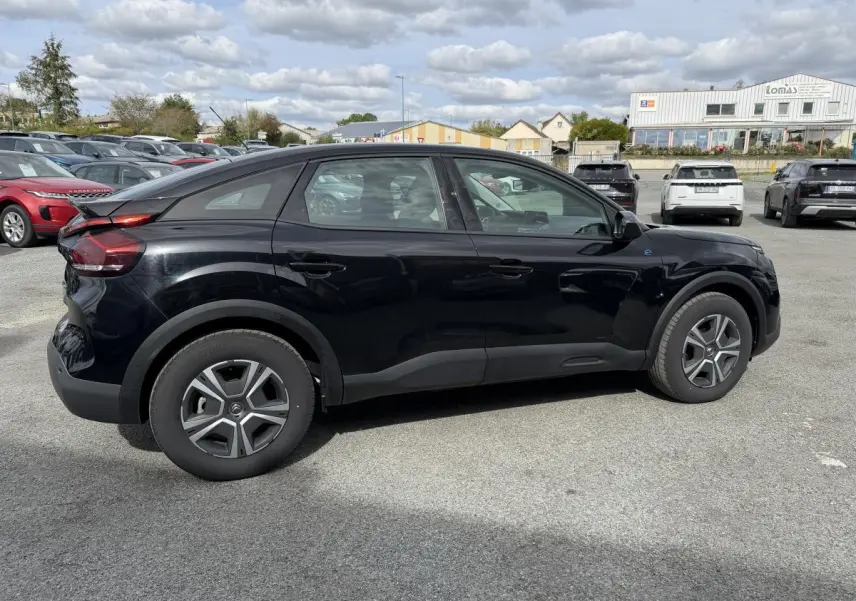 Profil droit d'une Citroën C4 électrique noire avec inserts noir brillant sur un parking extérieur.