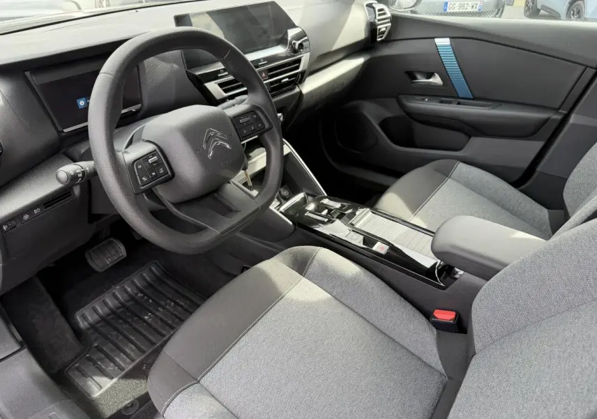 Intérieur avant droit de la Citroën C4 ë-136 2025, tableau de bord noir avec inserts bleus et sièges tissu gris.