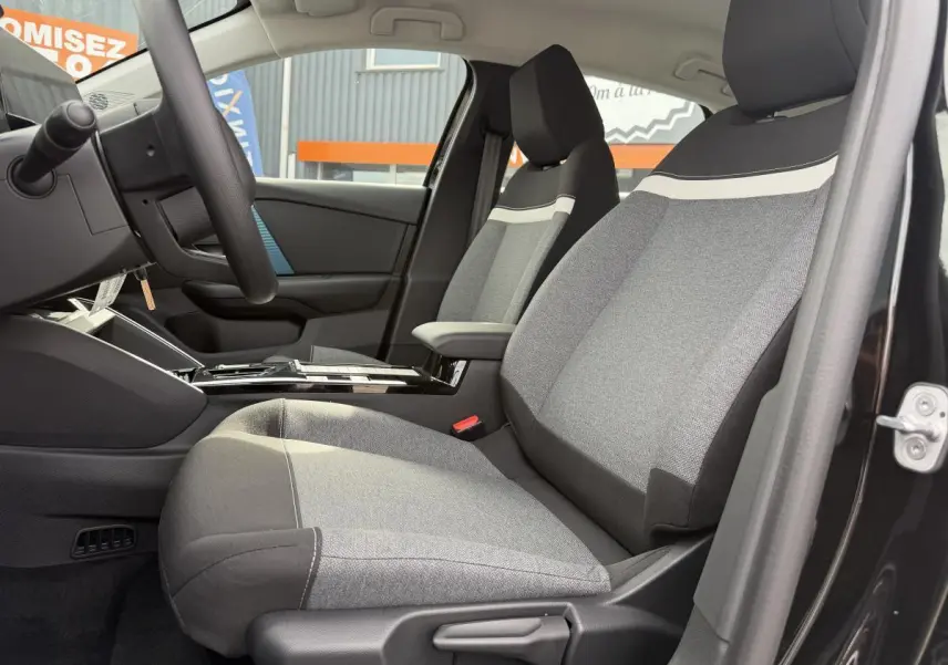 Vue intérieure côté conducteur de la Citroën C4 ë-136 2025, sièges tissu gris avec bande blanche, porte noire ouverte.