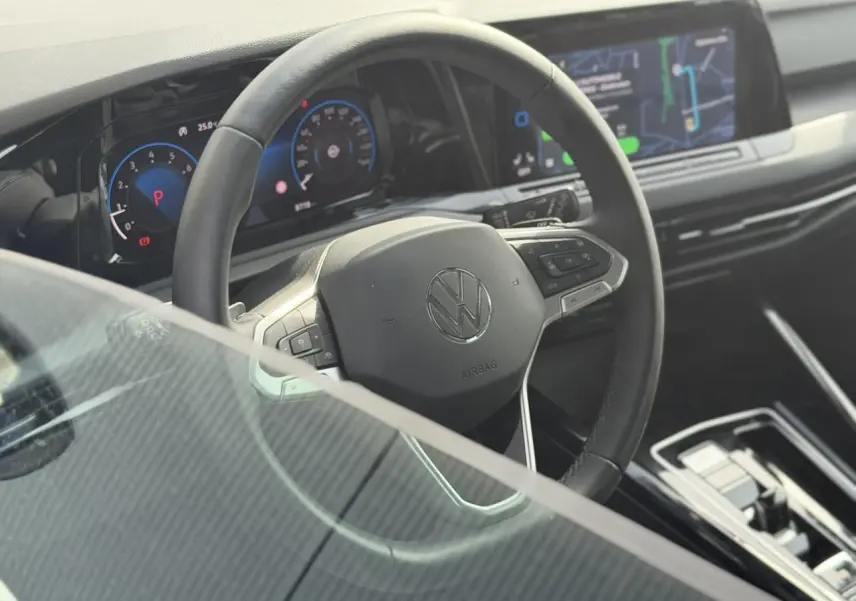 Vue intérieure centrée sur le volant multifonctions cuir de la Volkswagen Golf VIII 2024 avec tableau de bord numérique.