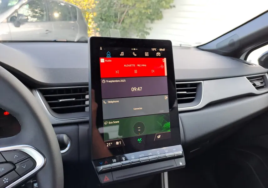 Vue intérieure du tableau de bord du Renault Captur 2025, avec écran tactile central affichant radio et climatisation.