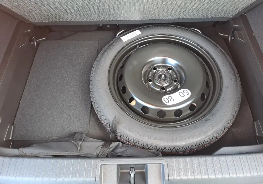 Vue plongeante sur la roue de secours noire dans le coffre du Renault Captur blanc nacré toit gris Highland 2025.