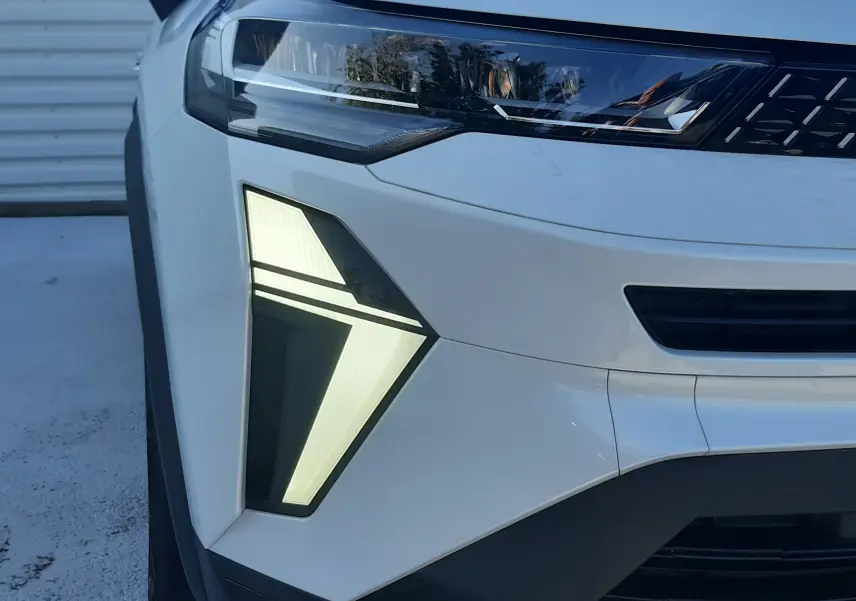 Gros plan sur l'avant gauche du Renault Captur blanc nacré avec feux LED en forme triangulaire et calandre noire.