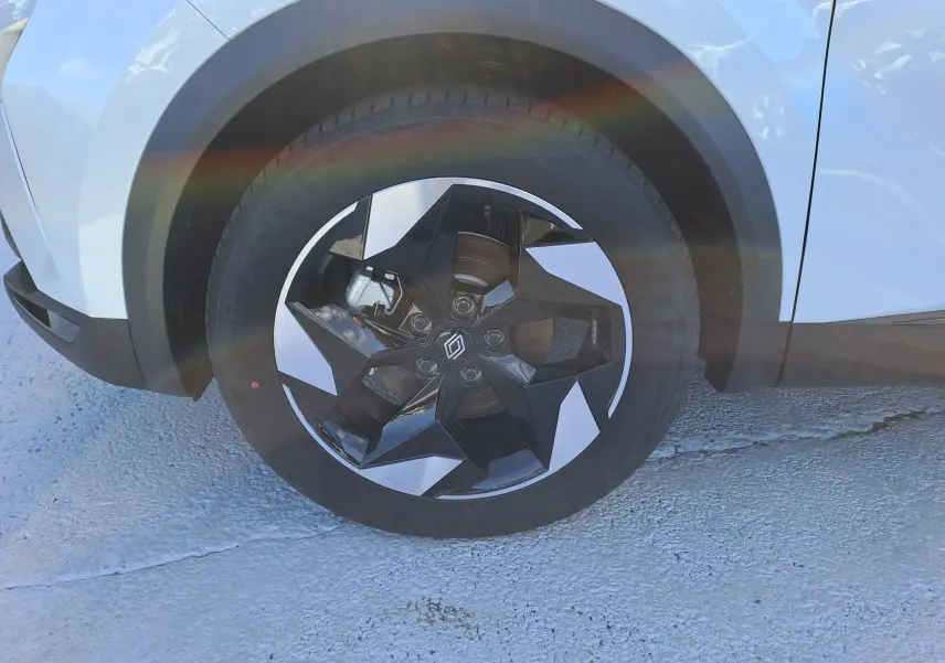 Gros plan sur la roue avant droite du Renault Captur blanc nacré avec jante noire et argentée au design géométrique.