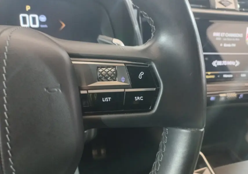 Gros plan sur les commandes gauche du volant cuir noir du DS7 Crossback 2021 avec écran tactile en arrière-plan.