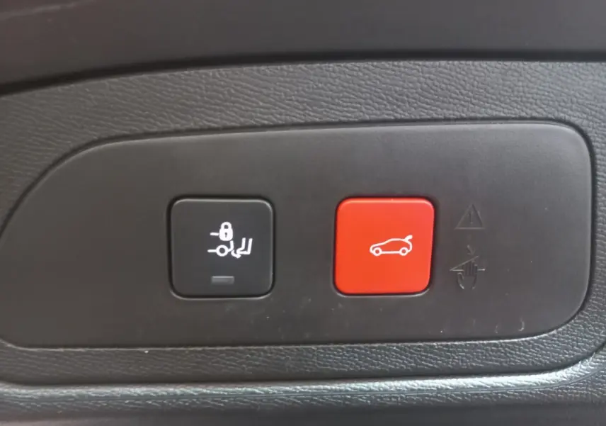 Gros plan sur les boutons de commande du coffre électrique, noir et rouge, intérieur d’un DS7 Crossback gris foncé.