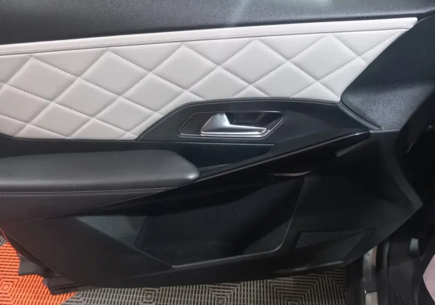 Gros plan sur la porte intérieure côté droit du DS7 Crossback gris foncé, avec cuir matelassé blanc et poignée argentée.